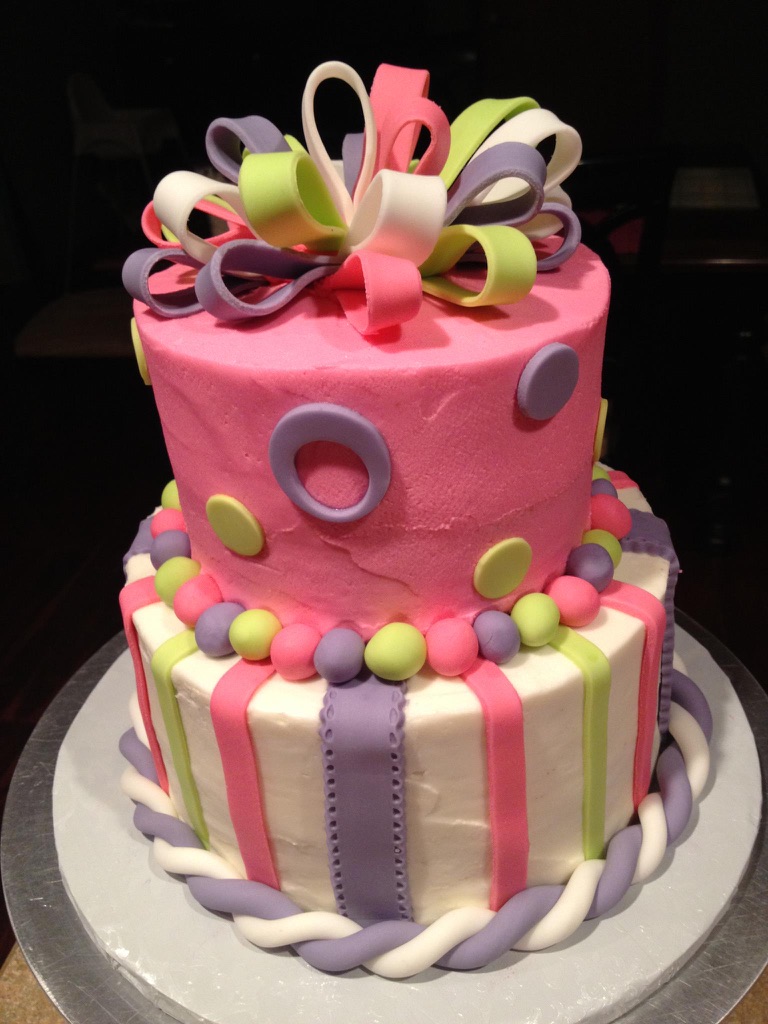 Two-tier pink and white cake with fondant stripes, polka dots and a looped bow topper