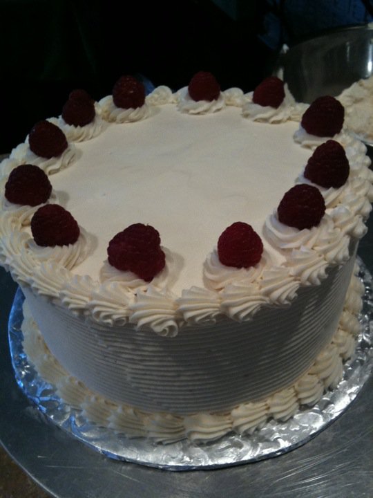 Round white buttercream cake crowned with fresh raspberries
