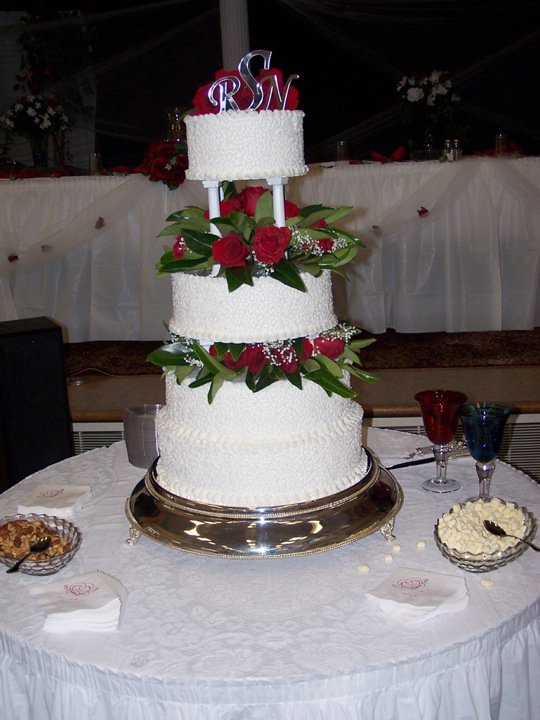 Four-tier white wedding cake on pillars with red roses between the tiers