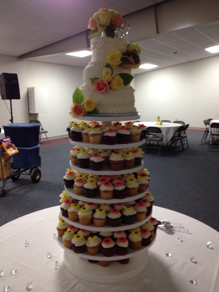 White wedding cake with pastel roses above a six-tier cupcake tower