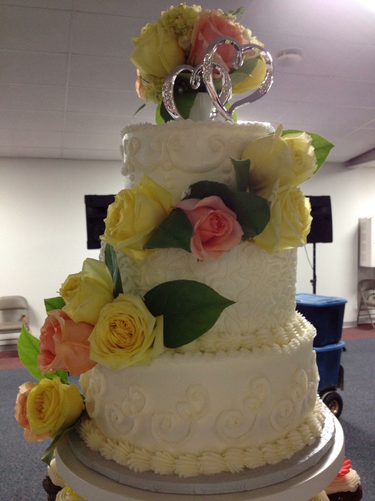 Three-tier white wedding cake with yellow and peach roses and a heart topper