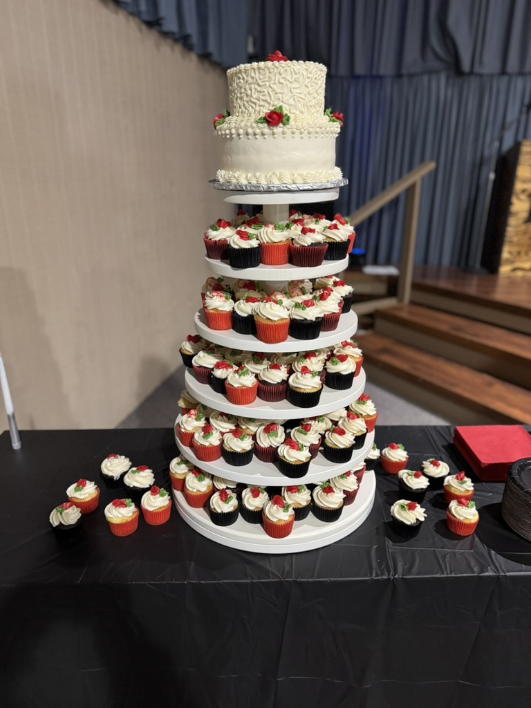 Two-tier white cake with red roses above a red and white cupcake tower