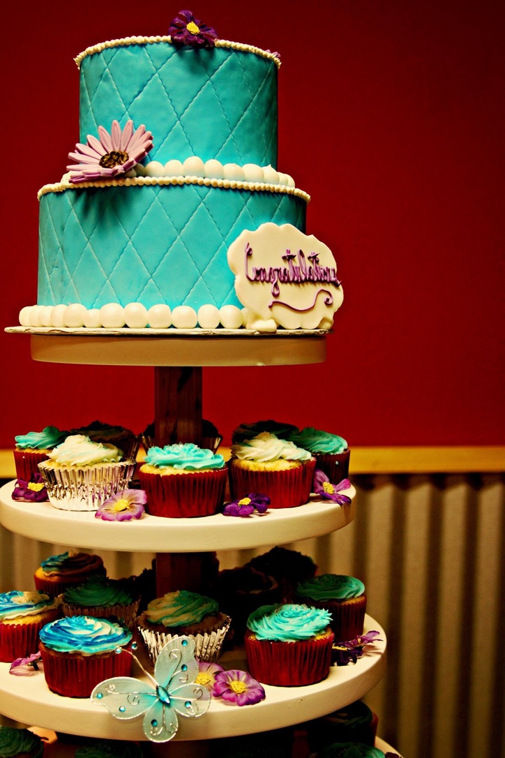 Turquoise quilted two-tier cake above a tower of cupcakes with sugar flowers