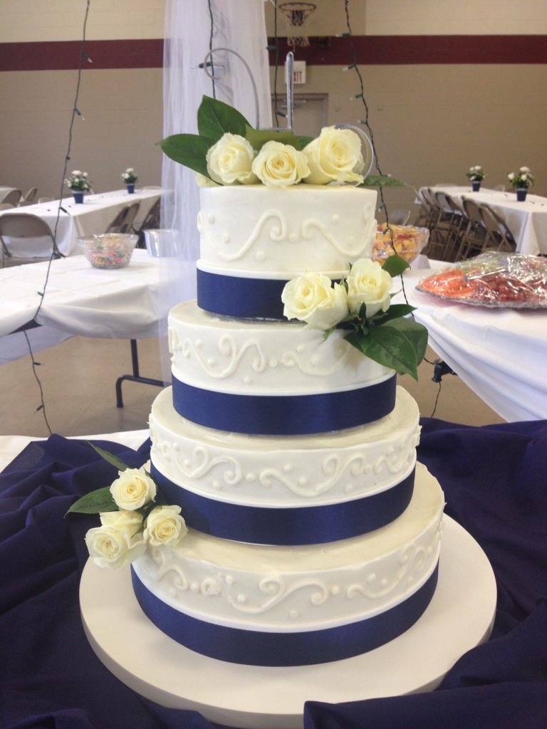 Four-tier white wedding cake with navy ribbon, scrollwork and ivory roses